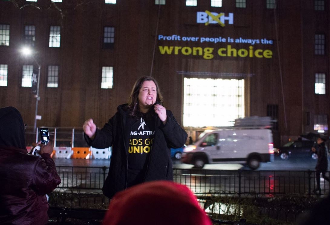 Damon in a black SAG-AFTRA Ads Go Union photo with projection on building behind her 'Profit over people is always the wrong choice'