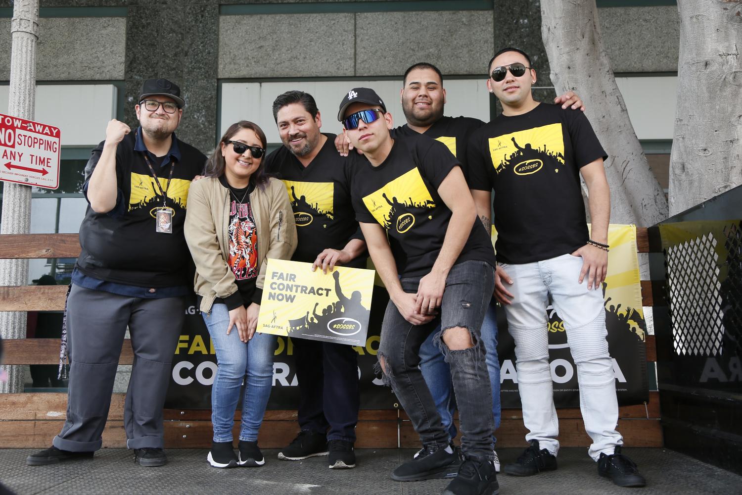 foto grupal de miembros de pie hombro con hombro sosteniendo un cartel amarillo de Contratos justos en el frente