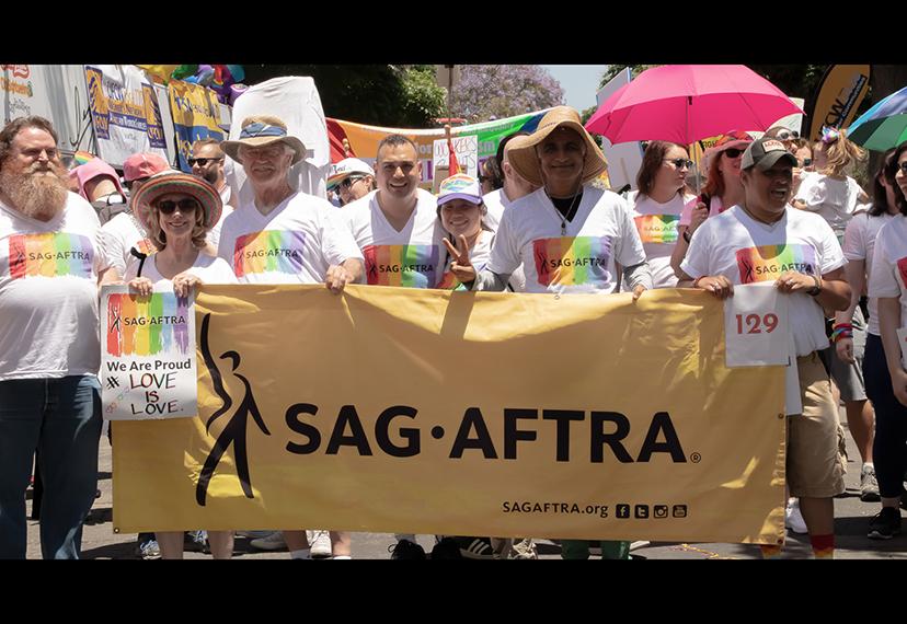 Miembros con camisas arcoiris SAG-AFTRA sosteniendo una pancarta amarilla SAG-AFTRA en el frente