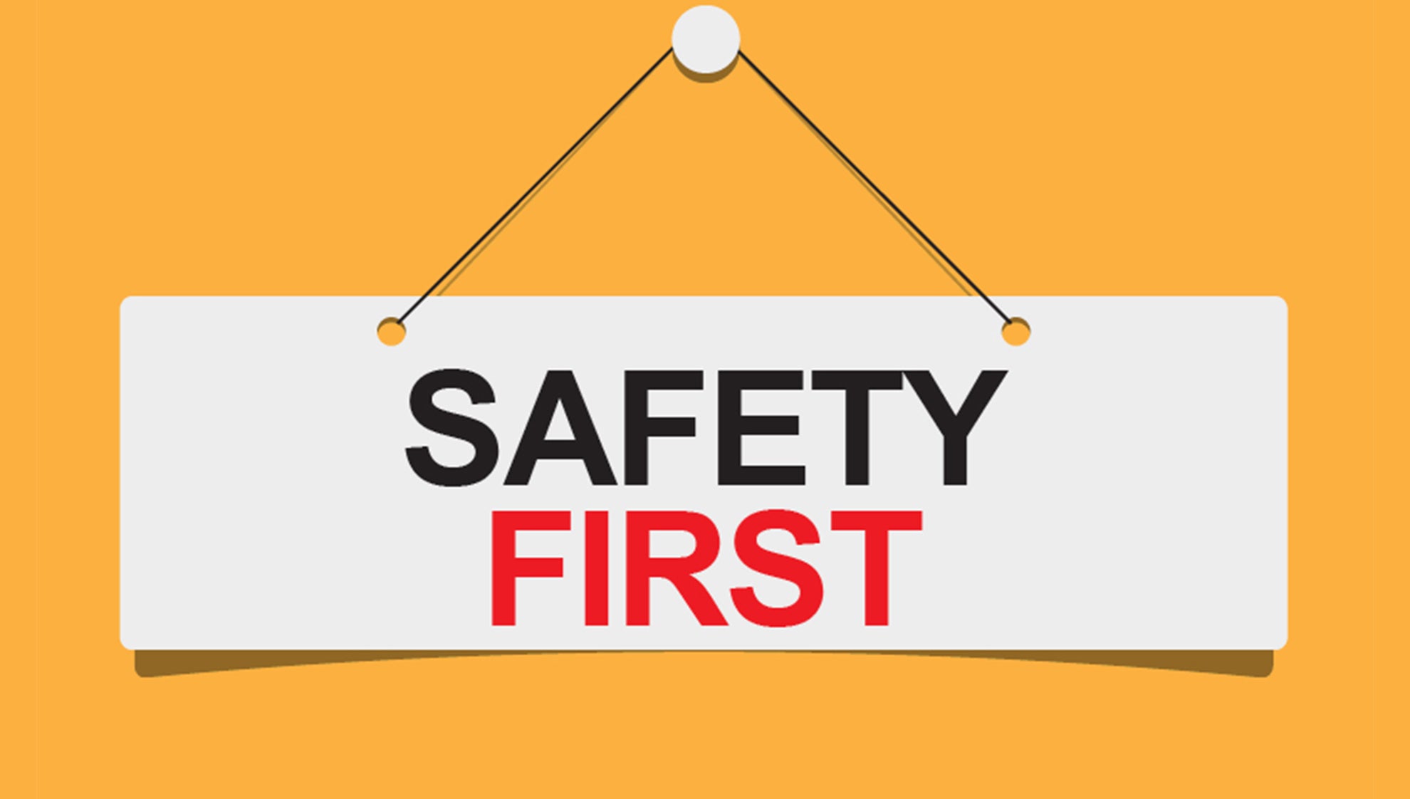 "Safety" in black "First" in red cursive on a white panel hanging from a whitepin with black string on a dandelion yellow background
