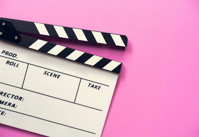 A picture of a film clapper with a pink background.