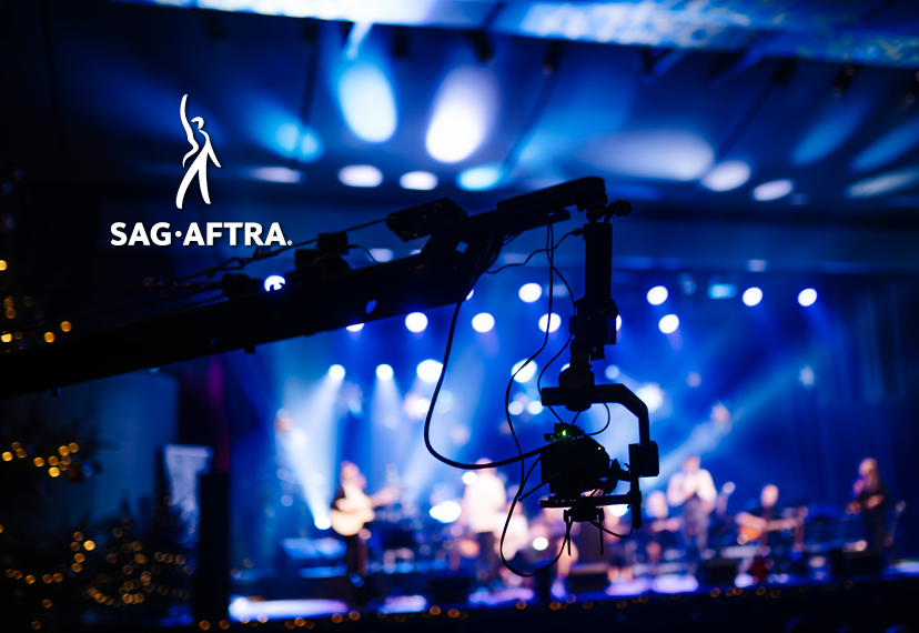 Fotografía de una cámara filmando un escenario con artistas en ella.