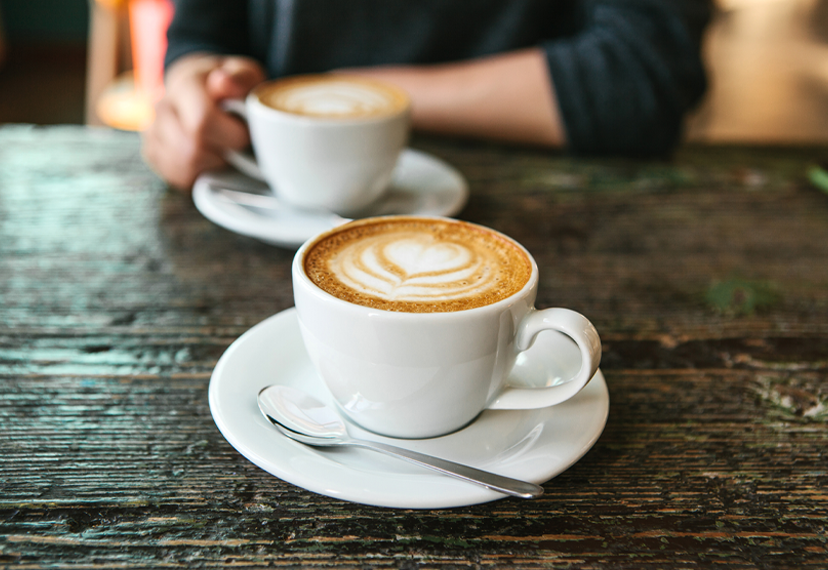 Photograph of two cups of coffee on a wooden table.