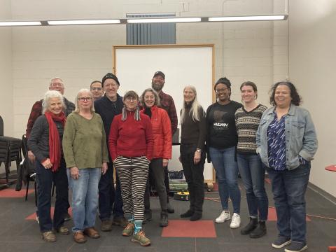 A group of SAG-AFTRA members gathers around instructor Mira Kehoe, third from right, at the conclusion of her most recent conservatory workshop. A group of smiling people, many wearing winter coats, hats and scarves pose for a photograph in a well-lit room.