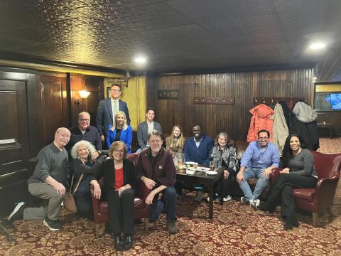 SAG-AFTRA broadcast members at WCCO-TV and members of the Twin Cities Local Board gather to celebrate the recent ratification of their new contract. A group of smiling people, some seated on couches and chairs, some standing, smile as they pose for a photograph in a room with dark wood paneling.