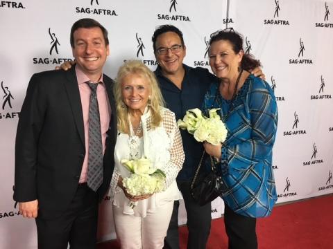 The Michigan Delegation poses for a photograph at the 2017 SAG-AFTRA convention. From left: Eric Wydra, Jo-Jo Shutty-MacGregor, Peter Tocco, Patty Handysides Two men and two women in business attire pose for a photo in front of a white banner with SAG-AFTRA logo. All are smiling and happy, the two women are holding bouquets of white flowers