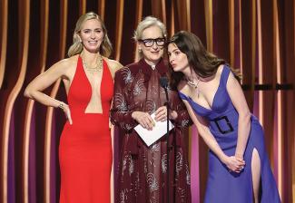 From left, Emily Blount, Meryl Streep and Anne Hathaway on stage. Hathaway leans into the stage microphone.