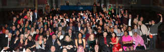 Un gran grupo de más de 150 personas sonríe para una foto grupal dentro de un cine.
