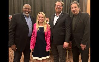 From left, Williamson (Black), Izanec, Bauder and Pronko stand for a group photo. Williamson, Bauder and Pronko wear suits; Izanec wears a pink blazer over a white dress. Some attendees are partially visible.