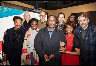 A group of diverse individuals stand, smiling, towards the camera. 