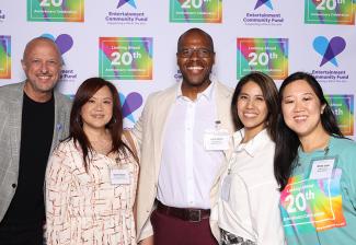 People of all ages and ethnicities wearing various clothing styles posing in front of a Looking Ahead 20th Anniversary/Entertainment Community Fund step-and-repeat backdrop.