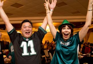 Two SAG-AFTRA members, one male and one female, wear Eagles football jerseys and smile at the party.
