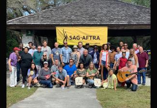 An outside photo of diverse group of men and women taken in front of a large, hanging banner of the union's logo.