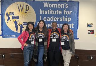 Four women stand against a wall in front of a blue banner that reads “Women’s Institute for Leadership Development.” They each wear SAG-AFTRA Pride T-shirts.