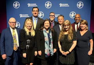 A group of nine people stand in two rows in front of a blue backdrop with the New Jersey State AFL-CIO logo in white.