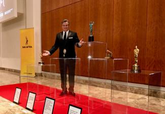 SAG-AFTRA Atlanta Local Board President Ric Reitz with outstretched arms stands with the EGOTS in the foreground.