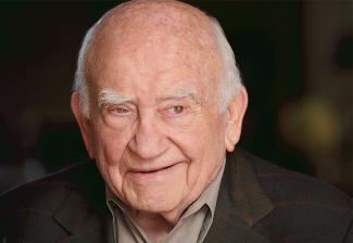 Asner in dark brown blazer smiling and looking off to the right