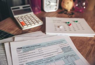 Image of tax forms with a calculator and calendar on a desk.