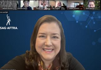 A screengrab of Damon smiling. She’s wearing a brown cardigan and a patterned scarf underneath. Her backdrop is blue with the SAG-AFTRA displayed in white. Above are smaller Zoom windows of other virtual participants. 