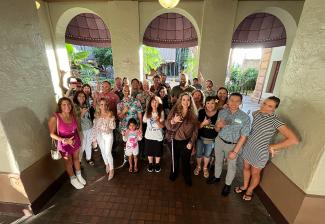 Un grupo grande y diverso afuera en un patio. Muchos en la foto hacen el gesto "shaka" con las manos.