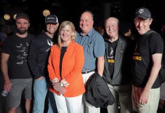 Seis personas, cinco hombres y una mujer, en una foto de grupo dentro de una habitación a oscuras. Dos hombres de extrema derecha visten camisetas negras "SAG-AFTRA Strong".