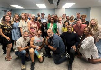 A diverse group of casually dressed people pose together in a classrom