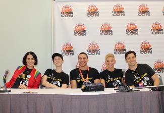 Five people, three women and two men, are seated at a dias. All wear SAG-AFTRA Video Game Strike T-shirts; the woman on the far left wears a bright red jacket and the woman beside her wears a ball cap. Behind them is a step-and-repeat backdrop with the L.A. Comic Con logo. 