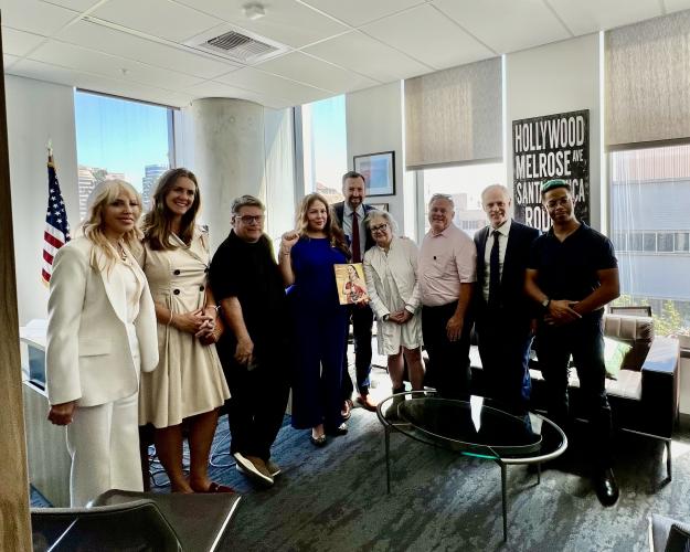 Una foto de grupo de nueve personas dentro del vestíbulo de una oficina. Allen, en el centro, está detrás de dos mujeres. Una mujer, la cuarta desde la izquierda, sostiene una copia de la revista 'SAG-AFTRA'.