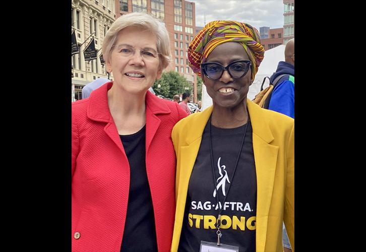 Warren lleva una blusa negra y un blazer rojo y está de pie junto a James con un pañuelo en el pelo de colores, vistiendo una chaqueta de traje amarilla, pantalones lisos y una camiseta negra que dice “SAG-AFTRA Strong”.