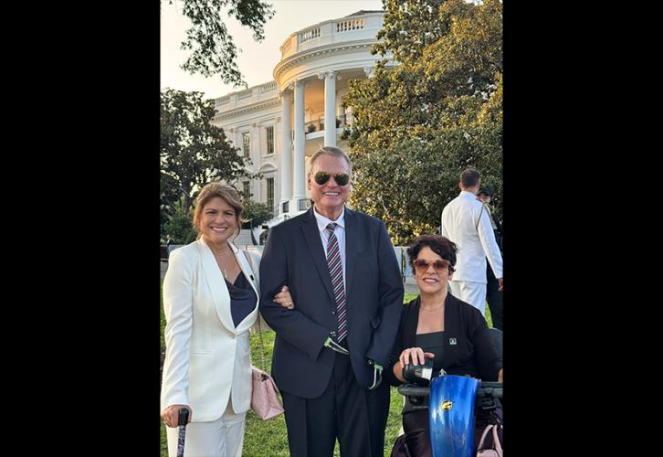Cyrille, Lawson y Bruno están afuera, en el jardín de la Casa Blanca. Lawson viste un traje negro con corbata a rayas, camisa blanca y gafas de sol. La Casa Blanca se ve al fondo, pero está oculta por los árboles.