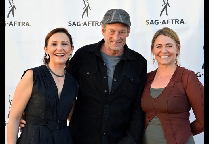 Three people smiling and standing in front of a banner with the SAG-AFTRA logo. 