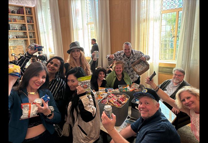 A group of people hold snacks in the air around a table.