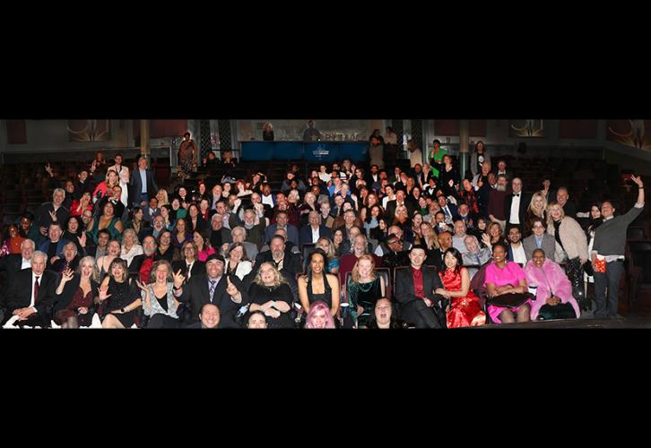 A large group smiles for a group photo inside a large movie theater.