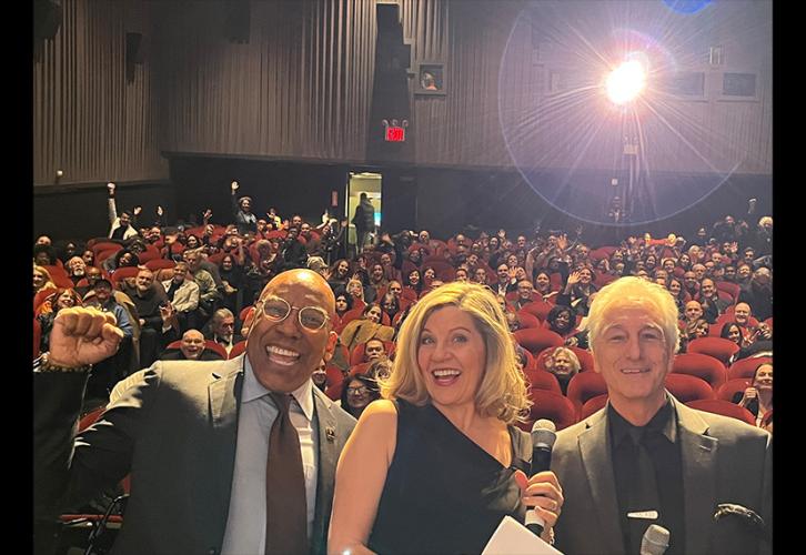 From left, Knight, Hammel and Baron are in the foreground. Knight raises his right fist. Behind them is a crowd seated in theater chairs. In the upper right corner is a glare from the projector.