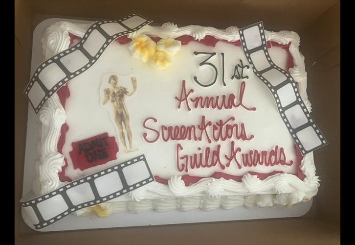 An image of a cake. It is decorated with film reel mouldings, popcorn pieces, a movie ticket and a cutout of the award statuette.