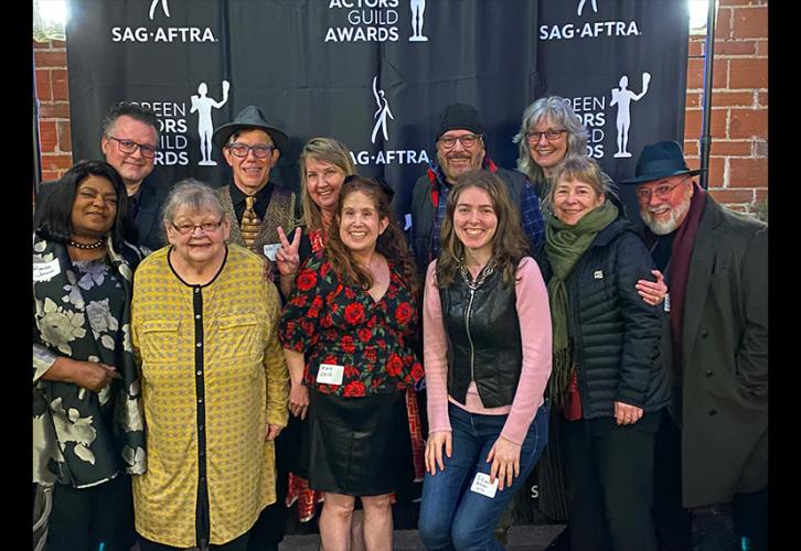 A group of 11 individuals take a photo against a black step-and-repeat backdrop with the SAG-AFTRA and SAG Awards logos. 
