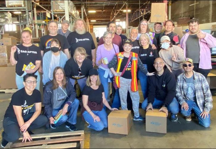 A group of individuals huddle together in a warehouse with boxes around them.