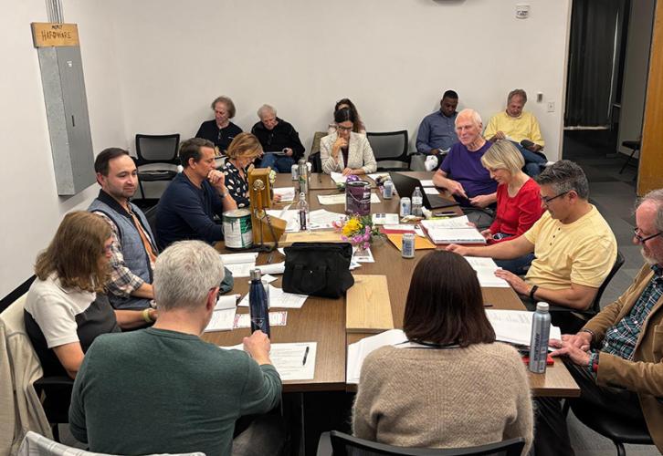 Individuals sitting around a wooden table reading scripts.