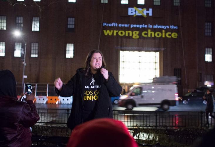 Damon in a black SAG-AFTRA Ads Go Union photo with projection on building behind her "Profit over people is always the wrong choice"