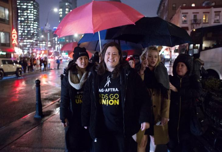 Damon in a black SAG-AFTRA #AdsGoUnion t-shirt under a red umbrella with members on her left and right. 