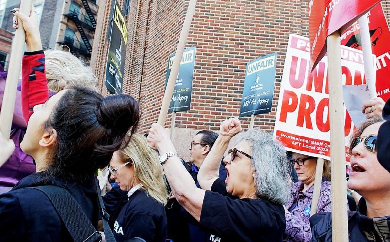 members and supporters hold up signs that reads "UNFAIR" in black text with a yellow background with the SAG-AFTRA Ads Go Union logo centered below. "ON STRIKE AGAINST" in yellow and "BBH Ad Agency" below it in white text all on a black honeycomb backgrou