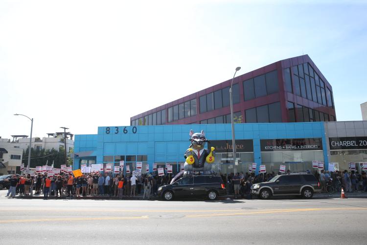 Group of people gathered outside on a street corner holding signs saying "UNFAIR, SAG-AFTRA on strike against BBH Ad Agency"