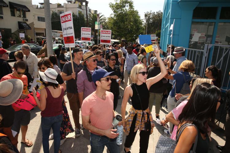 Group of people gathered outside on a street corner holding signs saying "UNFAIR, SAG-AFTRA on strike against BBH Ad Agency"