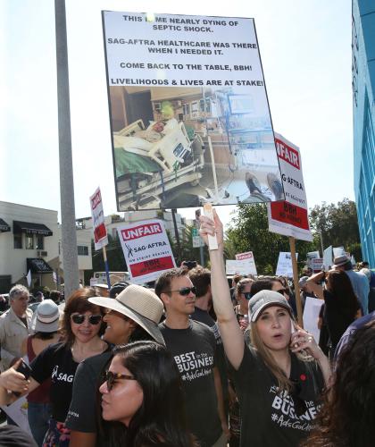 Group of people gathered outside on a street corner holding signs saying "UNFAIR, SAG-AFTRA on strike against BBH Ad Agency"