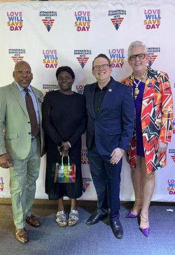 From left, Knight (Black) wears a green pants suit; Emma wears a black dress and silver sandals and holds a rainbow-colored bag; Crabtree-Ireland is in a dark blue suit; and Forest wears a bright and boldly patterned blazer over a blue dress.