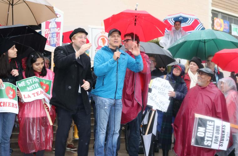 Fabian in a blue rain coat and a microphone in hand with a ASL interpreter on his right