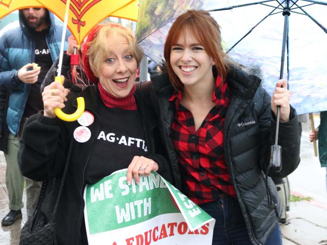 Crawford holding an umbrella and a "I stand with LA Educators" sign next to McLaughlin holding a clear umbrella