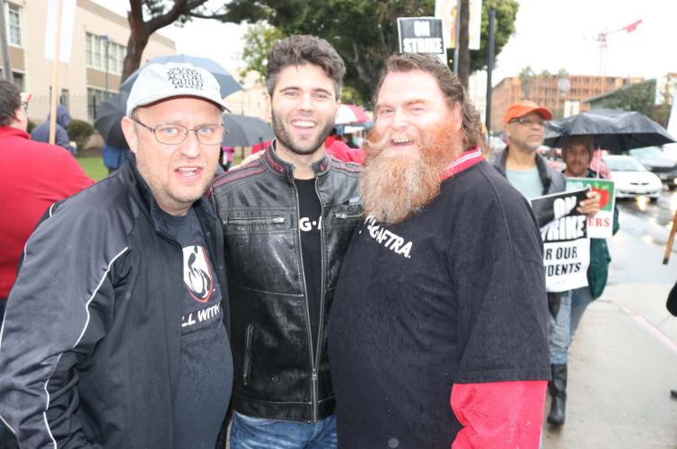 3 members posing for a photo with the crowd of protesters in the background 
