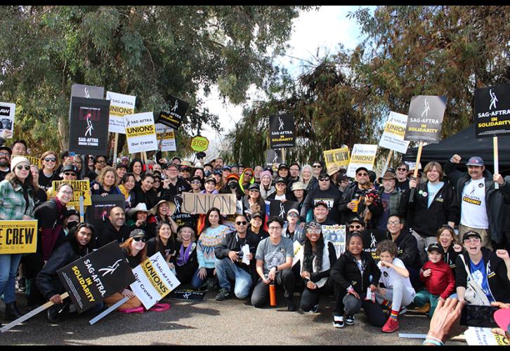 A photo of over 100  people of various ethnicities wearing various SAG-AFTRA shirts and posing with solidarity signs.