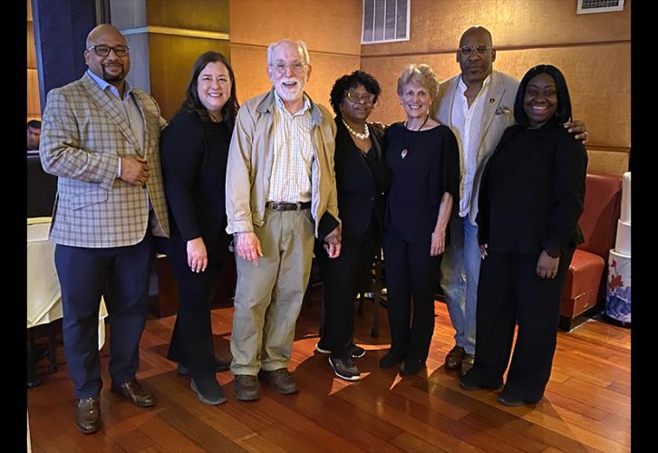 From left, Vincent (Black), Damon, Stanley, Luke-Stuart (Black), Karas, Knight (Black) and Bailey (Black) take a photo together in a lobby. The group stands in a single row. The lighting is low.